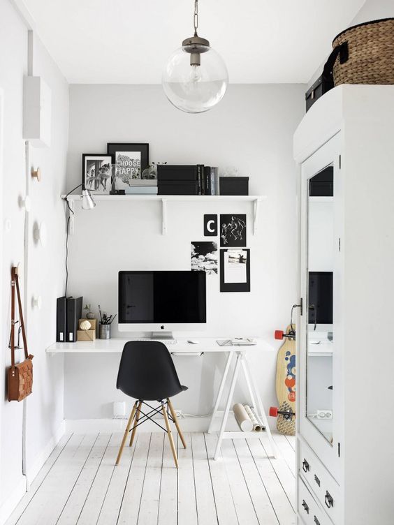 a black and white Scandinavian home office with a white trestle desk, a black chair, a white shelf and black decor, a glass pendant lamp