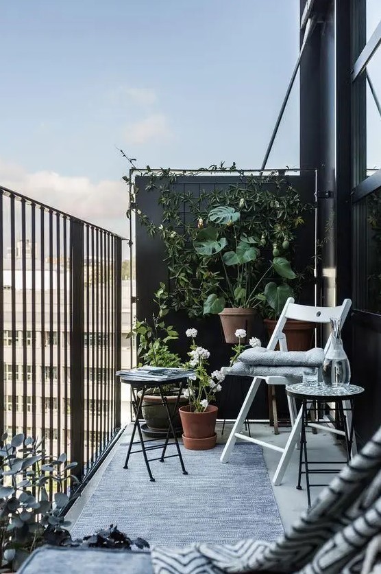 a black balcony done with a couple of folding chairs and a small coffee table plus a lot of greenery around