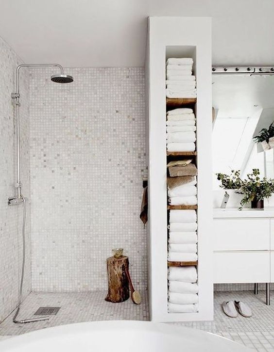 a chic and serene Scandinavian bathroom done in white and off-white, with a wooden stump, potted greenery and built-in storage