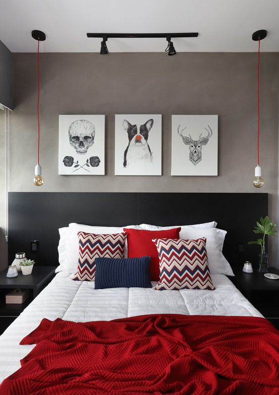 a chic modern bedroom with grey limewashed walls, a black bed with black, navy and white bedding, red pendant bulbs and a gallery of art