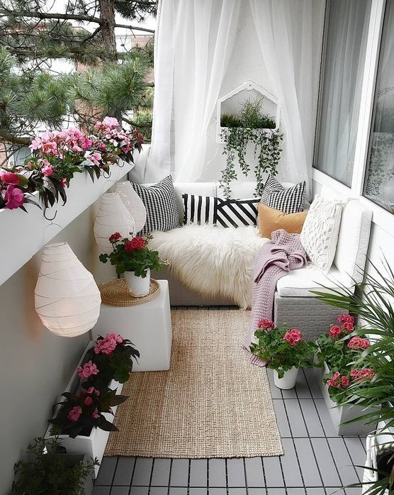 a chic yet small summer balcony in white, with sheer curtains, a jute rug, potted blooms, paper lanterns and printed textiles