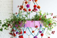 a colorful chandelier with greenery, bright pompoms, tassels and wooden beads is a cool decoration for any space