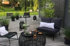 a contrasting Scandinavian terrace with black seating furniture, a black coffee table, a white umbrella and potted greenery