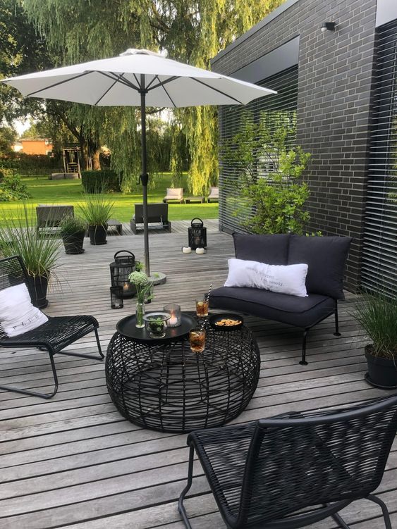 a contrasting Scandinavian terrace with black seating furniture, a black coffee table, a white umbrella and potted greenery a contrasting Scandinavian terrace with black seating furniture, a black coffee table, a white umbrella and potted greenery