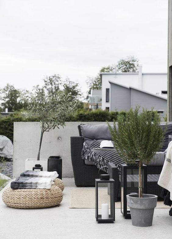 a contrasting Scandinavian terrace with black wicker furniture, a coffee table, potted greenery and jute poufs