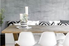 a cool Scandinavian dining space with a white storage bench with black and white pillows, a stained trestle table, white matching chairs and a black pendant lamp