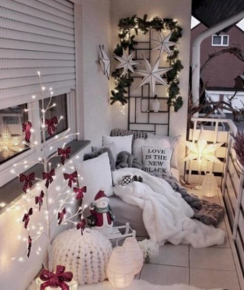 a cozy little balcony with a light tree with red bows, some candle lanterns, a star lamp, stars and greenery on the wall and fur and knit textiles