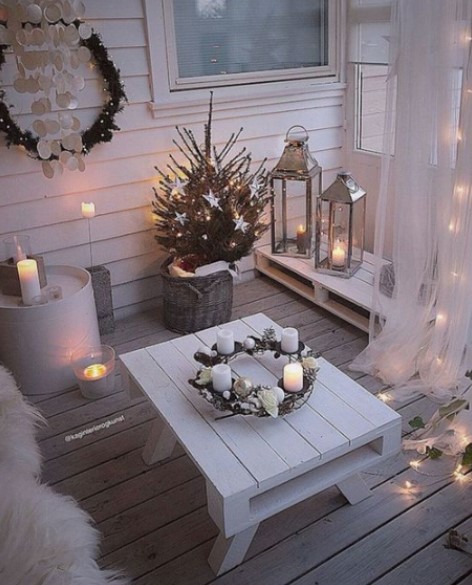 a cozy little winter balcony with shiplap furniture, faux fur, candles in candleholders and candle lanterns, a mini tree with stars and a wreath