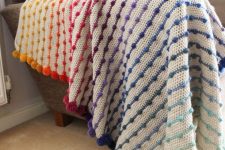 a crochet throw with colorful pompoms integrated is a very bright and fun accessory for your home