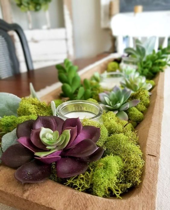 a dough bowl centerpiece with moss, succulents and candles in a glass candle holder is a trendy idea