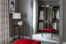 a gorgeous closet with grey walls, a large mirror in a tile frame, open wardrobes, a red upholstered bench and a coffee table