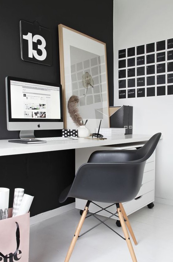 a laconic Nordic home office with a black statement wall and chair, a black noteboard, a white desk and a relaxed artwork