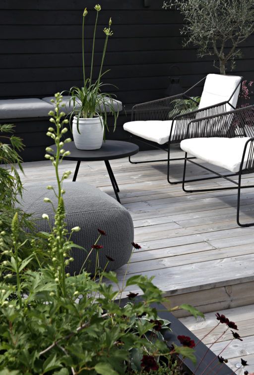 a laconic Nordic terrace with an upholstered bench, black and white chairs, a black coffee table and a grey pouf