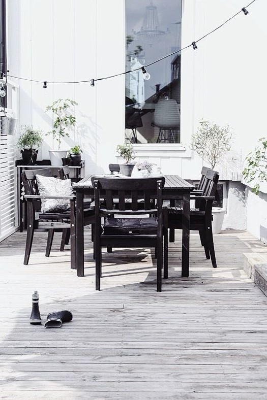 a laconic Nordic terrace with dark furniture, string lights and potted greenery plus all neutrals around