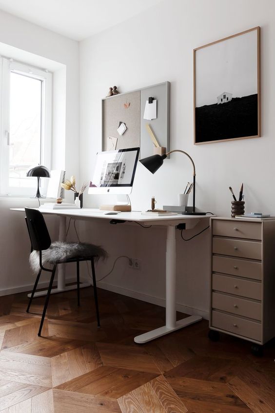a laconic Scandi home office with an IKEA desk, a black chair and lamps, a memo board, and an artwork, some decor