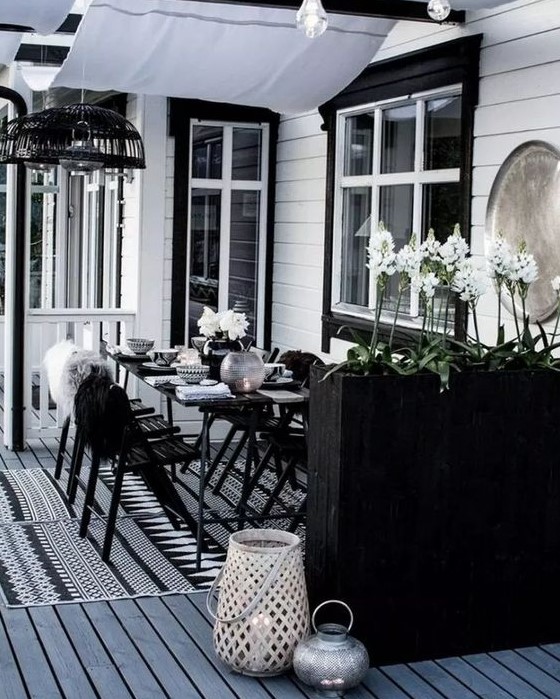a laconic Scandinavian dining space with black furniture, a tall planter as a space divider, candle lanterns and pendant lamps