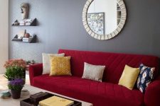 a living room featuring a grey accent wall, a deep red sofa with colorful pillows, a printed rug and a lovely coffee table
