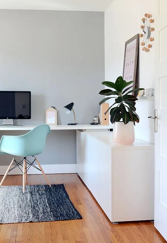 a lovely Scandinavian home office with a sleek storage unit and a built-in desk, a mint blue chair, potted greenery and a cool clock