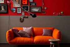 a lovely nook with a deep red and grey accent wall, an orange sofa, printed pillows, a catchy gallery wall and a wall sconce