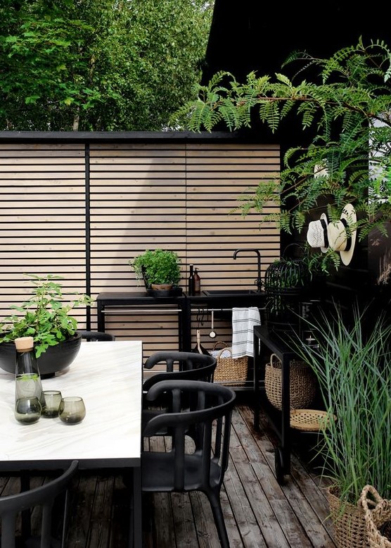 a modern Nordic terrace with a black kitchen space, black furniture, a white table and lots of greenery