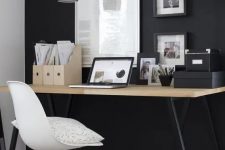 a modern Scandi space with a black wall, artworks and a wooden desk with black legs