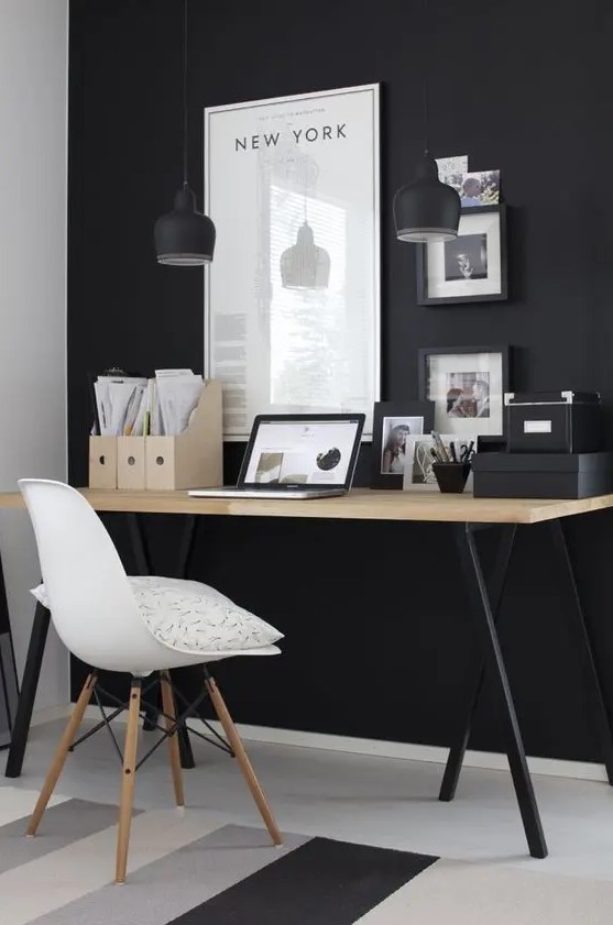 a modern Scandi space with a black wall, artworks and a wooden desk with black legs