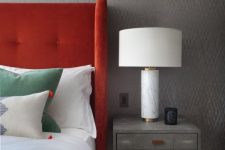 a modern bedroom with grey printed wallpaper, a grey nightstand with a chic table lamp, a bed with a bold red upholstered headboard