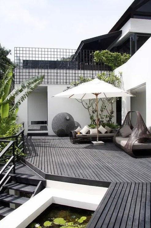 a monochromatic Scandinavian terrace with a black deck, dark rattan furniture, lots of greenery and a tree plus a little pond a monochromatic Scandinavian terrace with a black deck, dark rattan furniture, lots of greenery and a tree plus a little pond