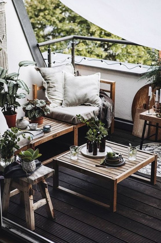 a monochromatic balcony with a black floor, natural wooden furniture, neutral textiles, potted greenery and candles