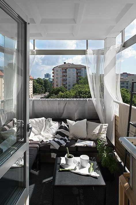 a monochromatic balcony with dark furniture, printed textiles, sheer curtains and potted greenery