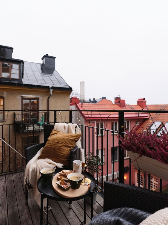 a moody Nordic balcony with black wicker chairs and a black coffee table, bold blooms and neutral and bright textiles and pillows