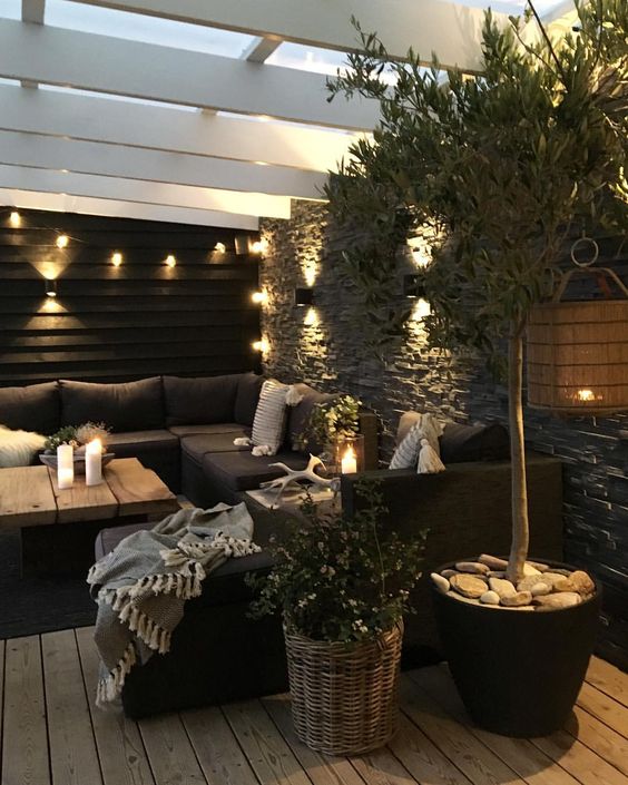 a moody Nordic terrace with a black sectional, a living edge coffee table, potted greenery and candle lanterns and string lights a moody Nordic terrace with a black sectional, a living edge coffee table, potted greenery and candle lanterns and string lights