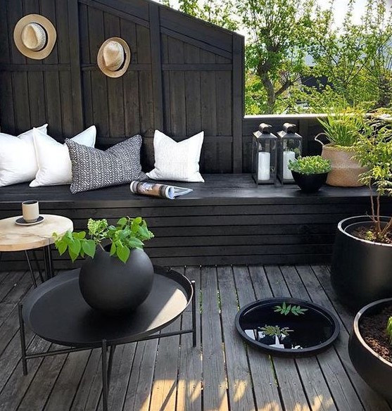 a moody terrace with black wood, light pillows, potted greenery and candle lanterns looks fresh and stylish