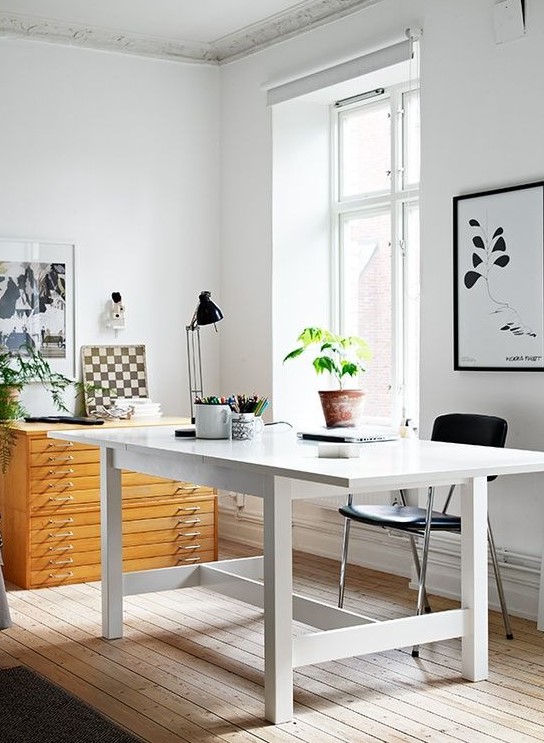 a neutral Scandinavian home office with a white desk, a wooden cabinet, some black and white art and a black chair