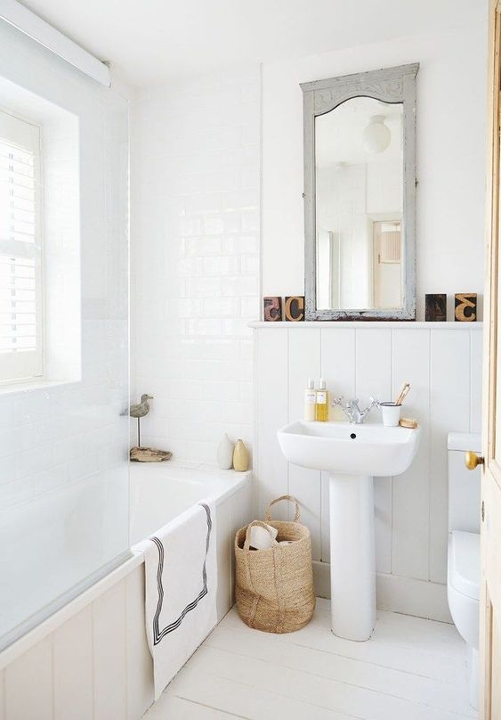 a neutral and cute bathroom with a Nordic feel, a basket for storage, a vintage mirror and whiet tiles