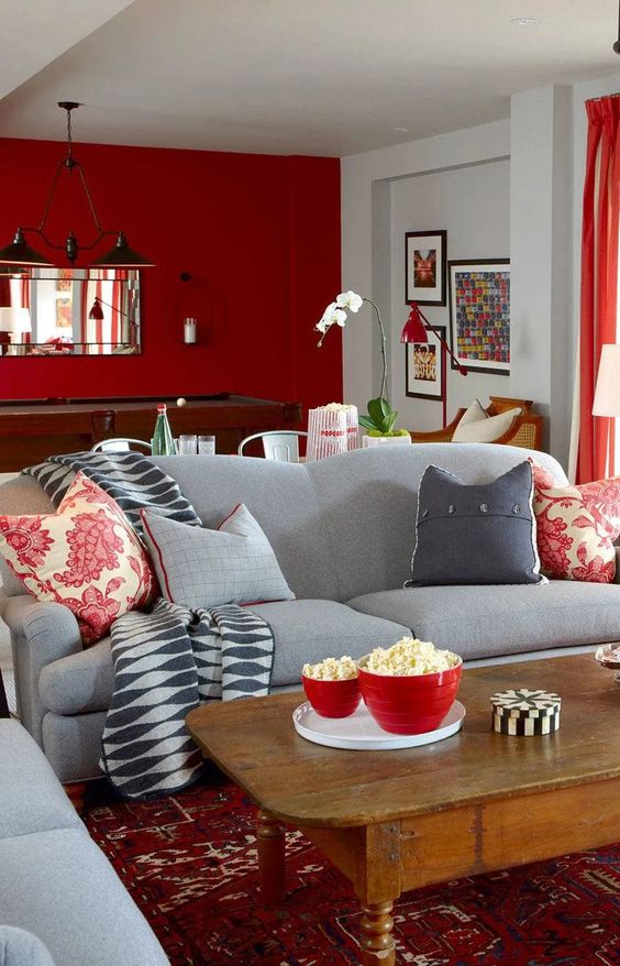 a pretty and bold living room with a deep red accent wall, a couple of grey sofas, printed textiles and a rug, a stained coffee table