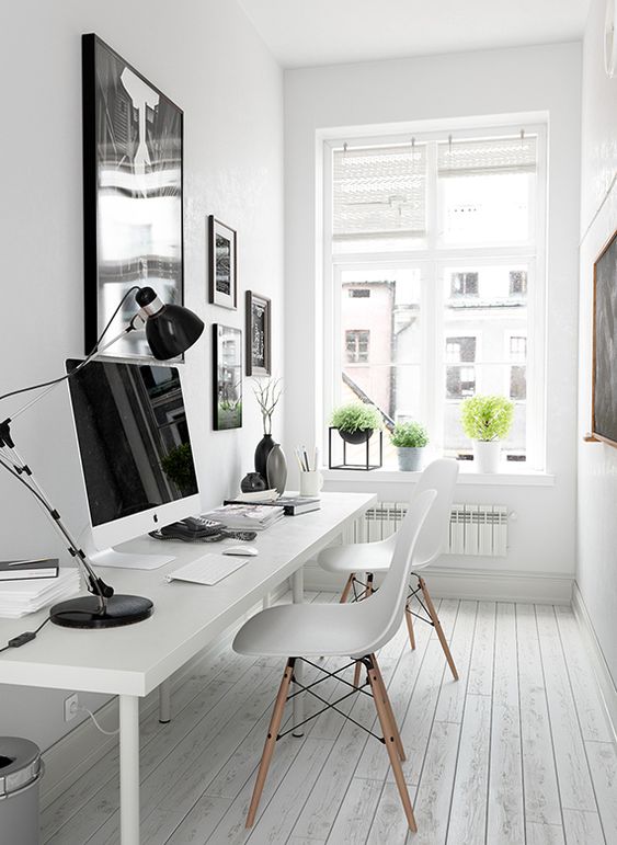 a pretty white Nordic home office with a black and white gallery wall, a white shared desk, white chairs and potted greenery