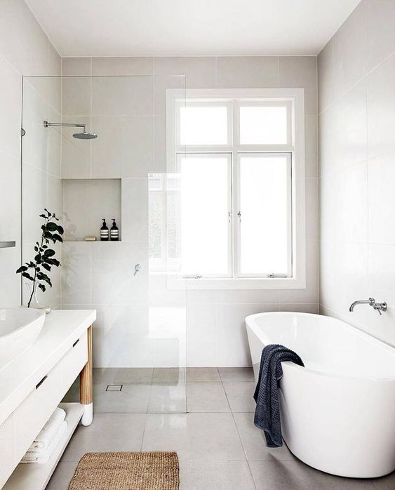 a refreshing Scandinavian bathroom with white walls, an oval tub, a long white vanity and a jute rug