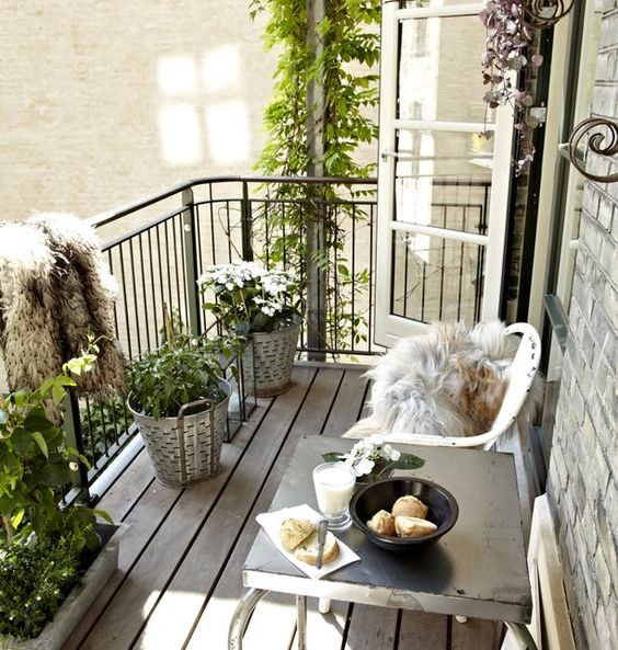 a relaxed Scandinavian balcony with white metal chairs and a metal table, potted greenery and blooms, faux fur covers is cool