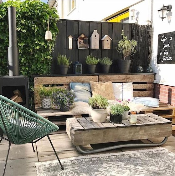 a rustic Scandinavian terrace with reclaimed wood furniture, a green chair, potted plants and birdhouses