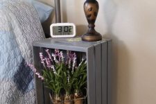 a rustic nightstand made of a crate and soem vintage legs, with blooms, a chic vintage table lamp and a clock is ideal for a rustic bedroom