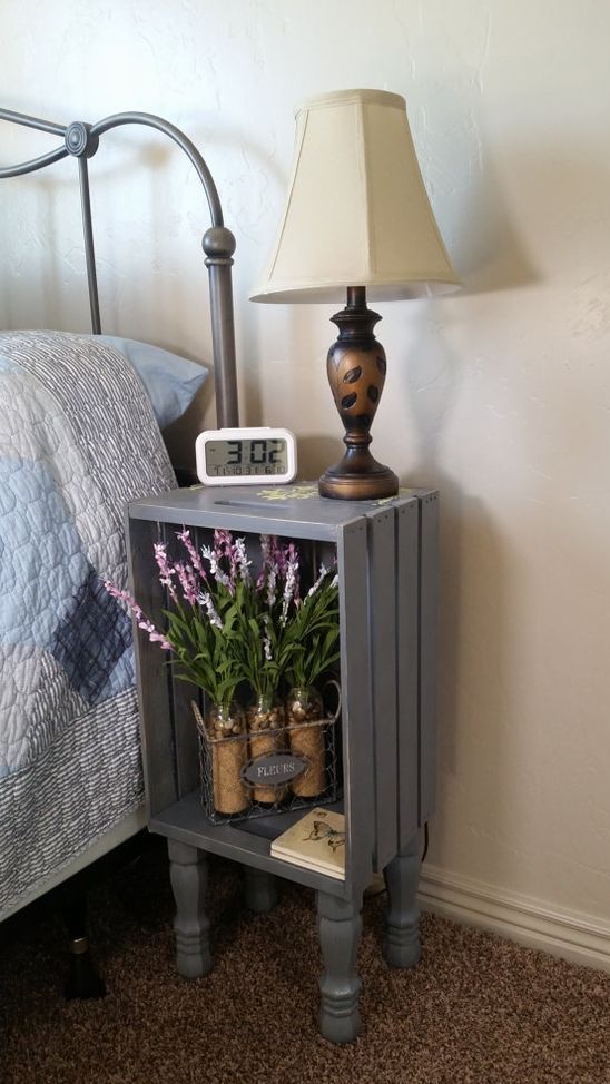 a rustic nightstand made of a crate and soem vintage legs, with blooms, a chic vintage table lamp and a clock is ideal for a rustic bedroom