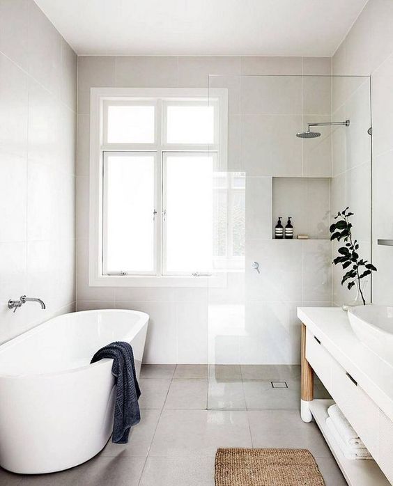 a serene Nordic bathroom with an oval tub, storage niches, a long vanity with a sink and potted greenery
