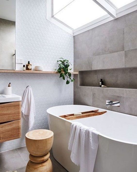 a serene Scandinavian bathroom with grey tiles, a white statement wall, much natural wood in decor and a skylight