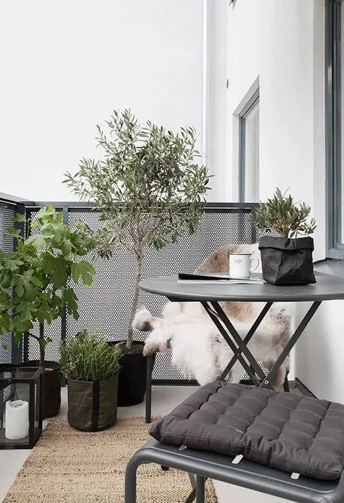 a simple and chic Scandinavian balcony with dark metal furniture, potted plants and trees, candle lanterns and faux fur