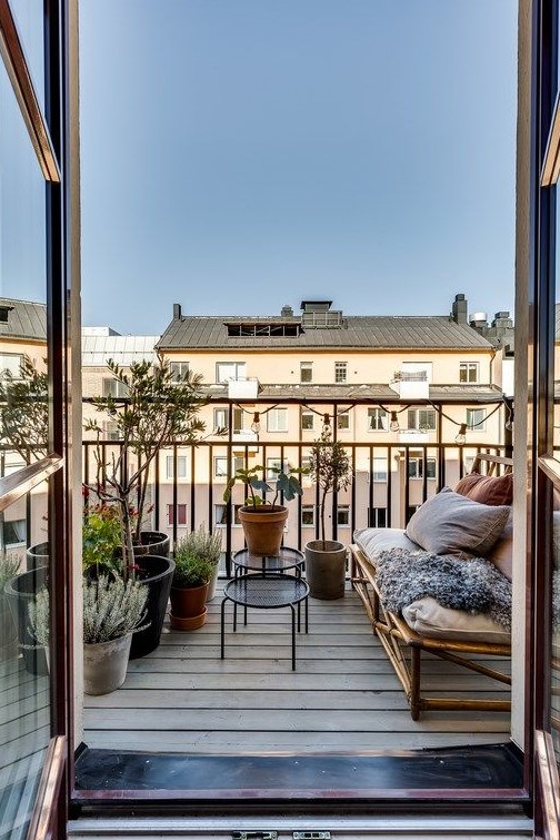 a simple and natural balcony with a rattan sofa, lots of pillows and blankets, potted greenery and other plants