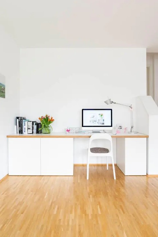 a small Nordic home office nook with a large desk with sleek storage units, a table lamp, some books and blooms is welcoming