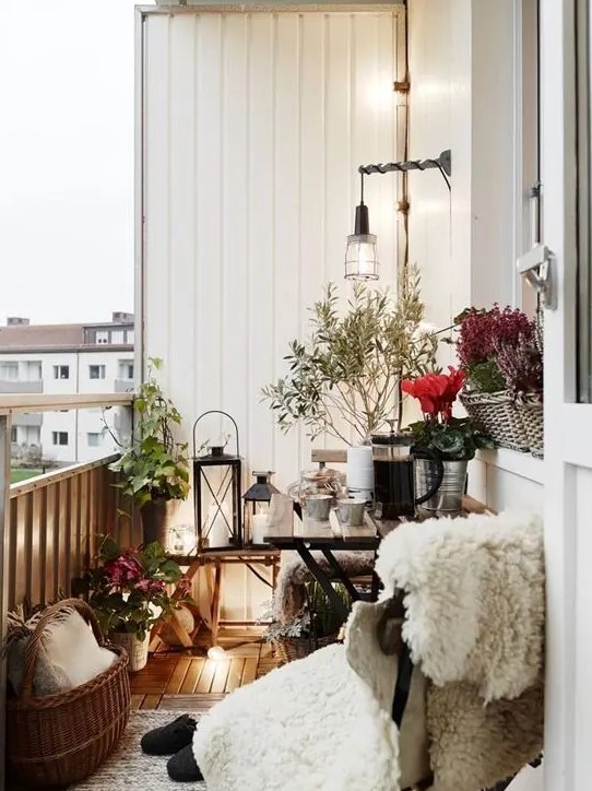 a small Scandinavian balcony with a chair covered up with faux fur, candle lanterns, baskets and planted flowers