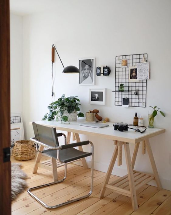 a small Scandinavian home office nook with a trestle desk, a black chair, a grid for memos, potted plants and a black sconce