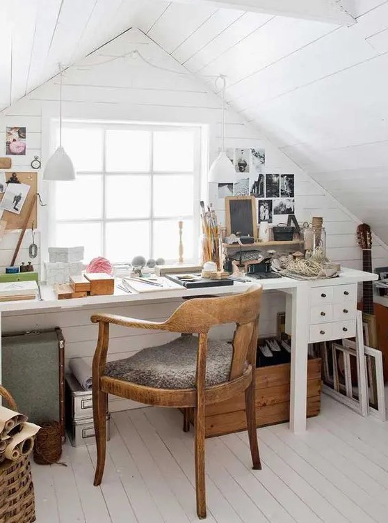 a small and cozy attic home office with white planked walls and a ceiling, a white desk with some drawers, a stained chair and some gallery walls